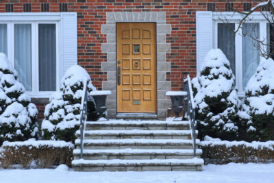 Traditional brick house with wood grain front door and snow covered shrubbery